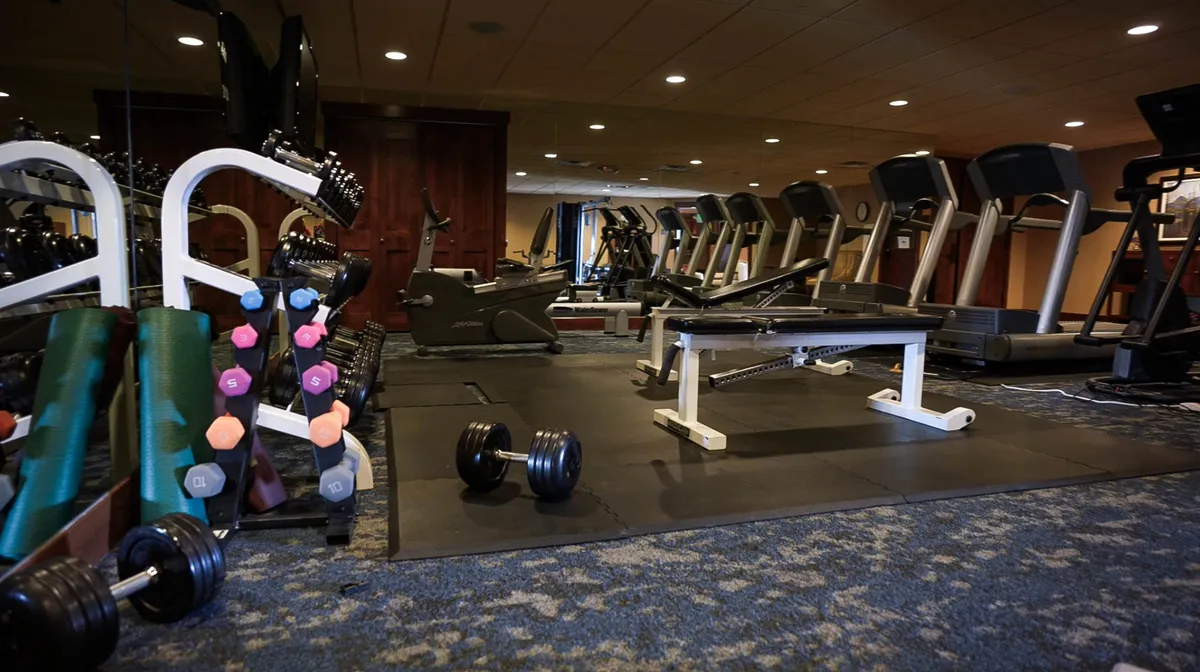 A well-equipped interior fitness center with dumbbells, treadmills, and a weight bench, bathed in natural light. The layout suggests both personal achievement and group motivation, reflecting an inviting and practical amenity for active guests.