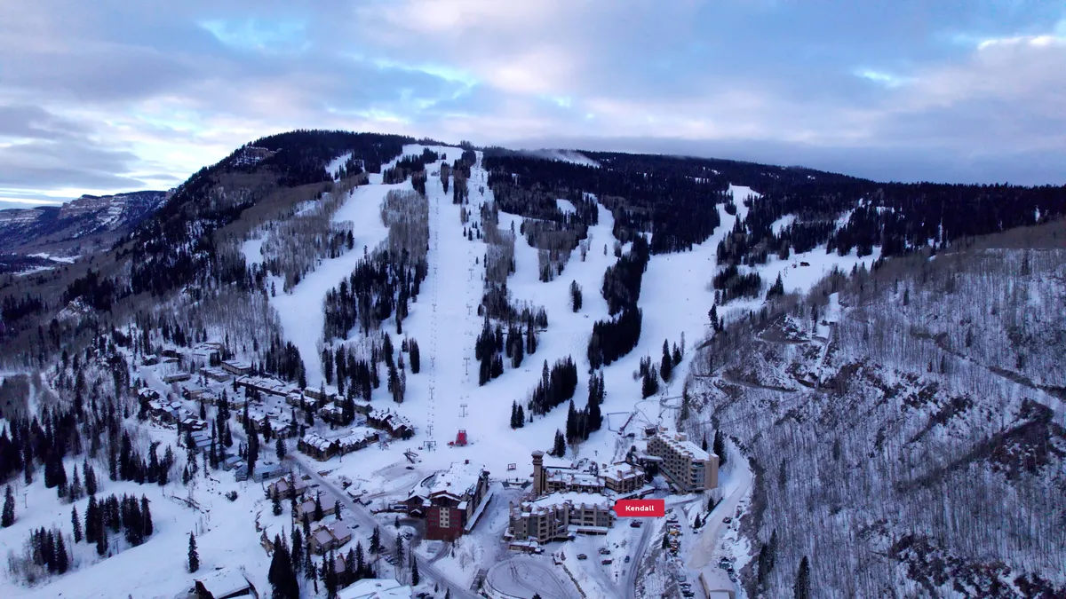 An inviting exterior scene showcasing the ski slopes, majestic mountains, and the cozy lodging buildings nestled at their base. The image captures the soft light of sunrise, hinting at both adventure and moments of peaceful relaxation. The atmosphere is one of both excitement and tranquility, perfectly attuned to a romantic mountain setting.