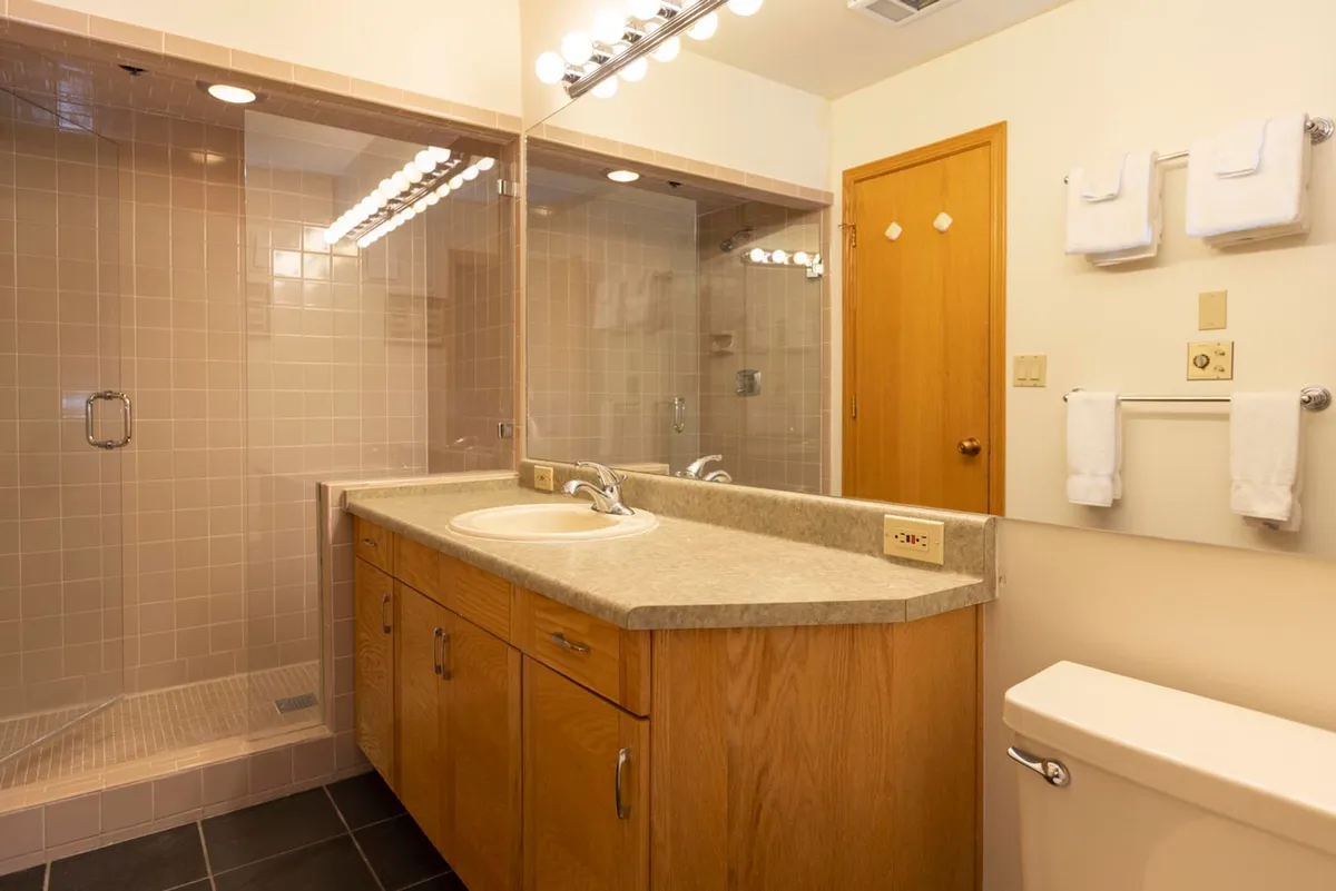 A well-appointed bathroom featuring a vanity with sink, large mirror, shower area, and wood cabinetry. The space is bright and practical, with ample storage and an inviting atmosphere for self-care routines.