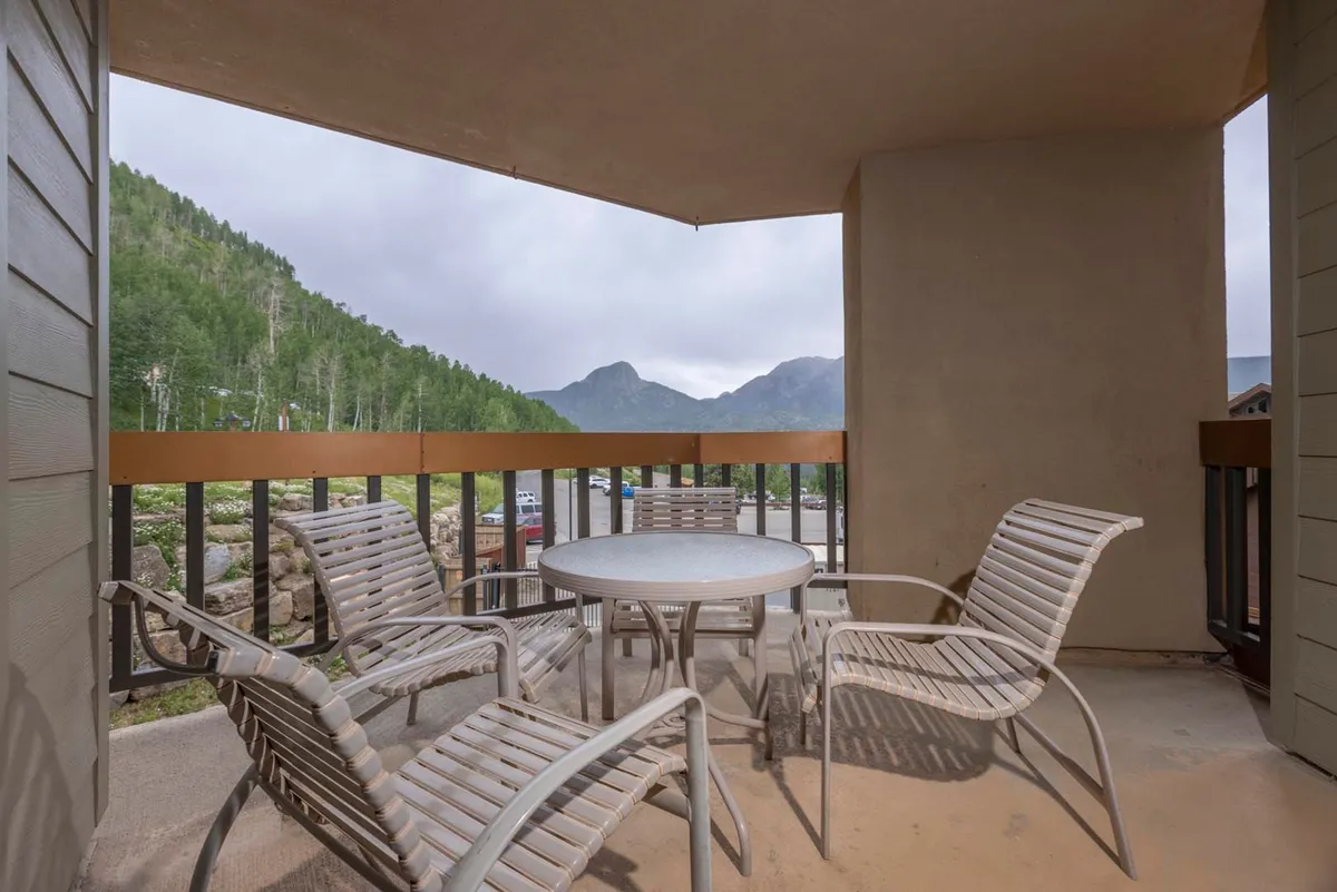 A serene outdoor dining setup on a balcony or patio, featuring a table and chairs that overlook sweeping mountain views. The calm, inviting mood suggests a perfect spot for families to gather after a day of adventure, enjoying meals with a breathtaking natural backdrop.