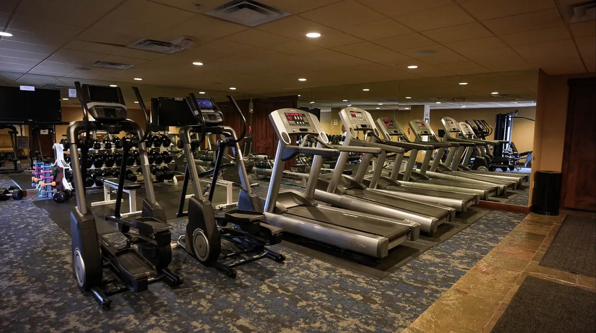 A bright, modern fitness center with treadmills, ellipticals, dumbbells, and a mirrored wall. The space feels energetic and well-equipped, ideal for both solo workouts and group fitness sessions.