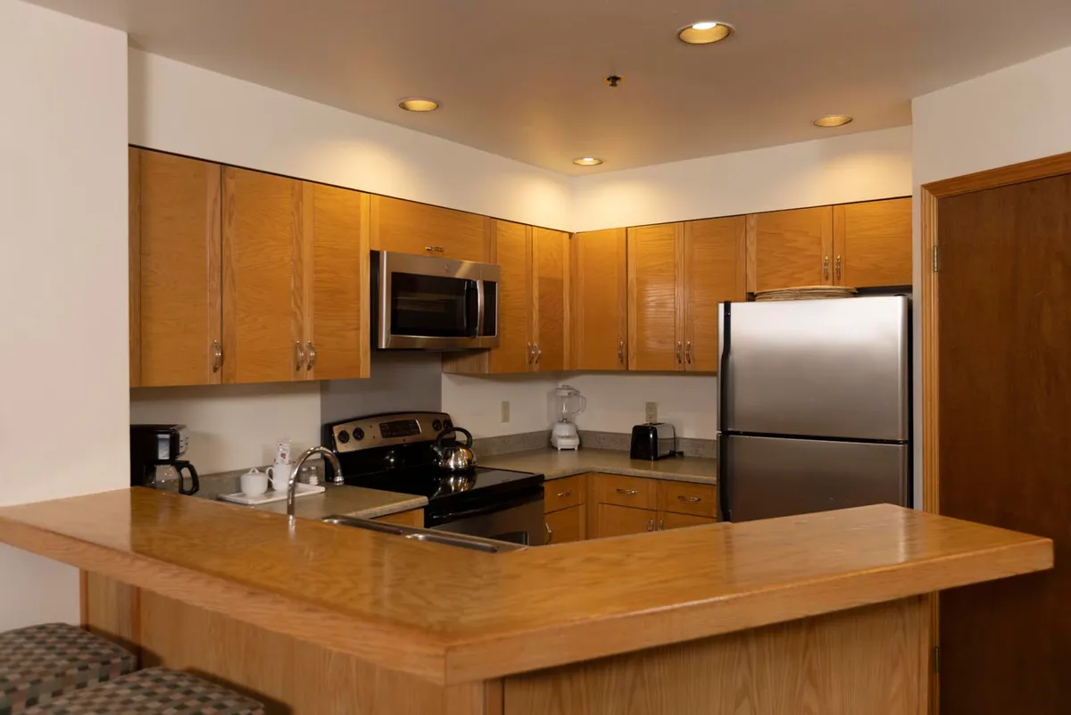 A stylish kitchen island stands at the center, surrounded by wood cabinetry and gleaming stainless steel appliances. The space feels warm and inviting, with clear cues for group cooking or a cozy breakfast gathering.